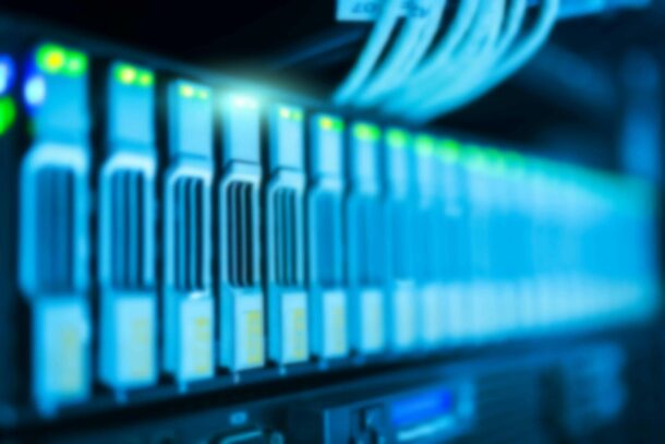 A row of blurred, illuminated server racks with network cables connected, indicating an active data center environment.