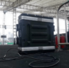 A large black equipment case with cables attached sits on a stage under a tent. Metal railings and a person in the background are visible. A large black equipment case with cables attached sits on a stage under a tent. Metal railings and a person in the background are visible.